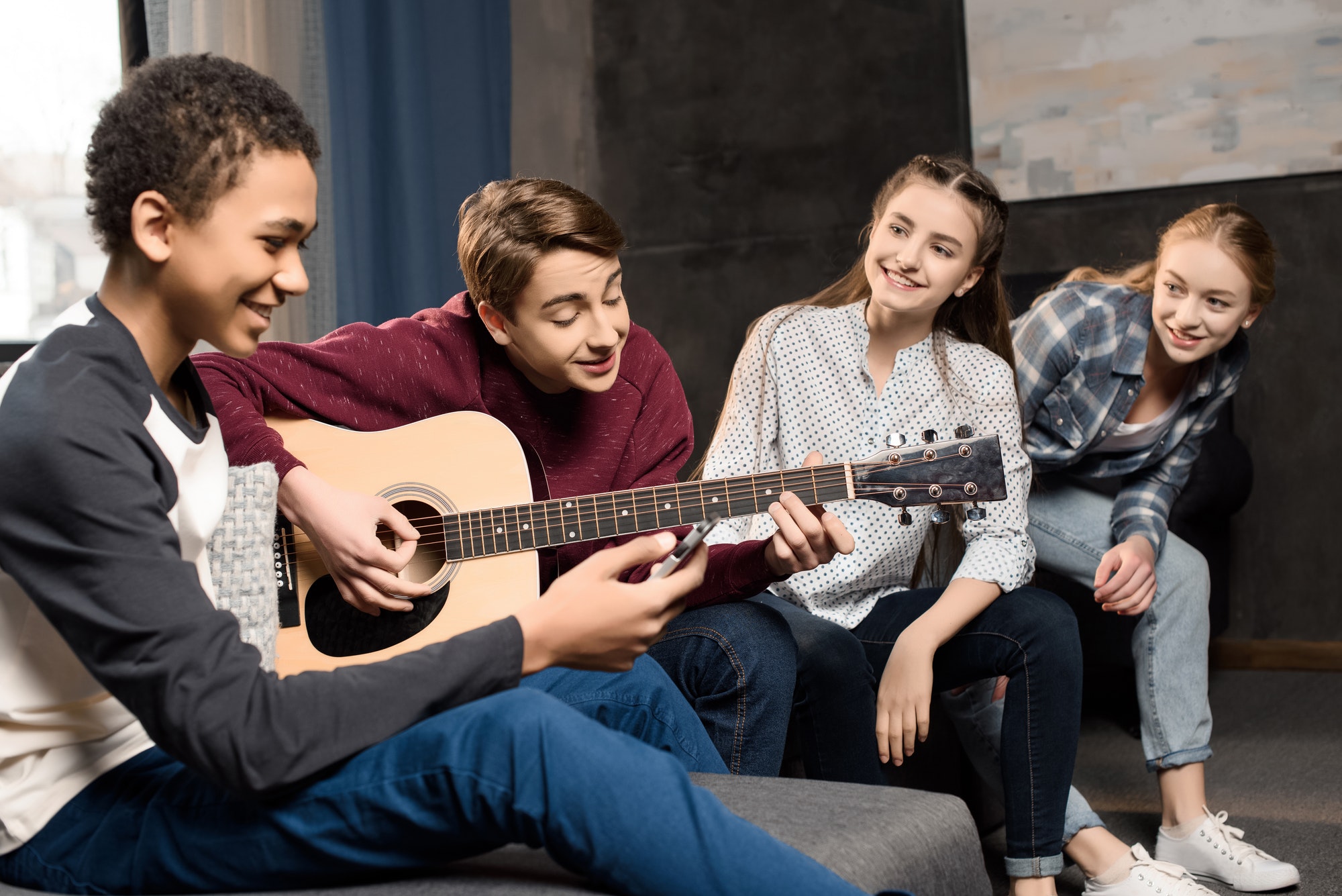 boy playing acustic guitar and singing while his friends listening at home, teenagers playing guitar