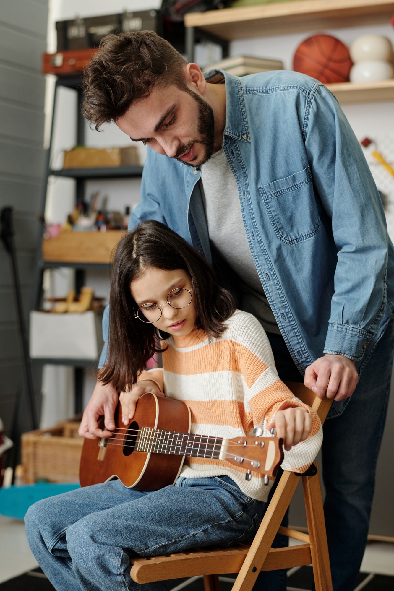 Cute little girl fitting strings of guitar before lesson of music with her tutor